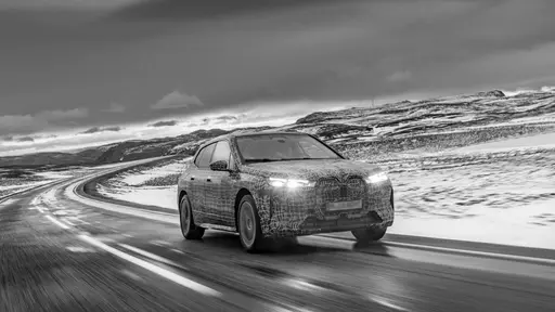 A car driving on a wet road with snow-covered hills in the background under a cloudy sky.